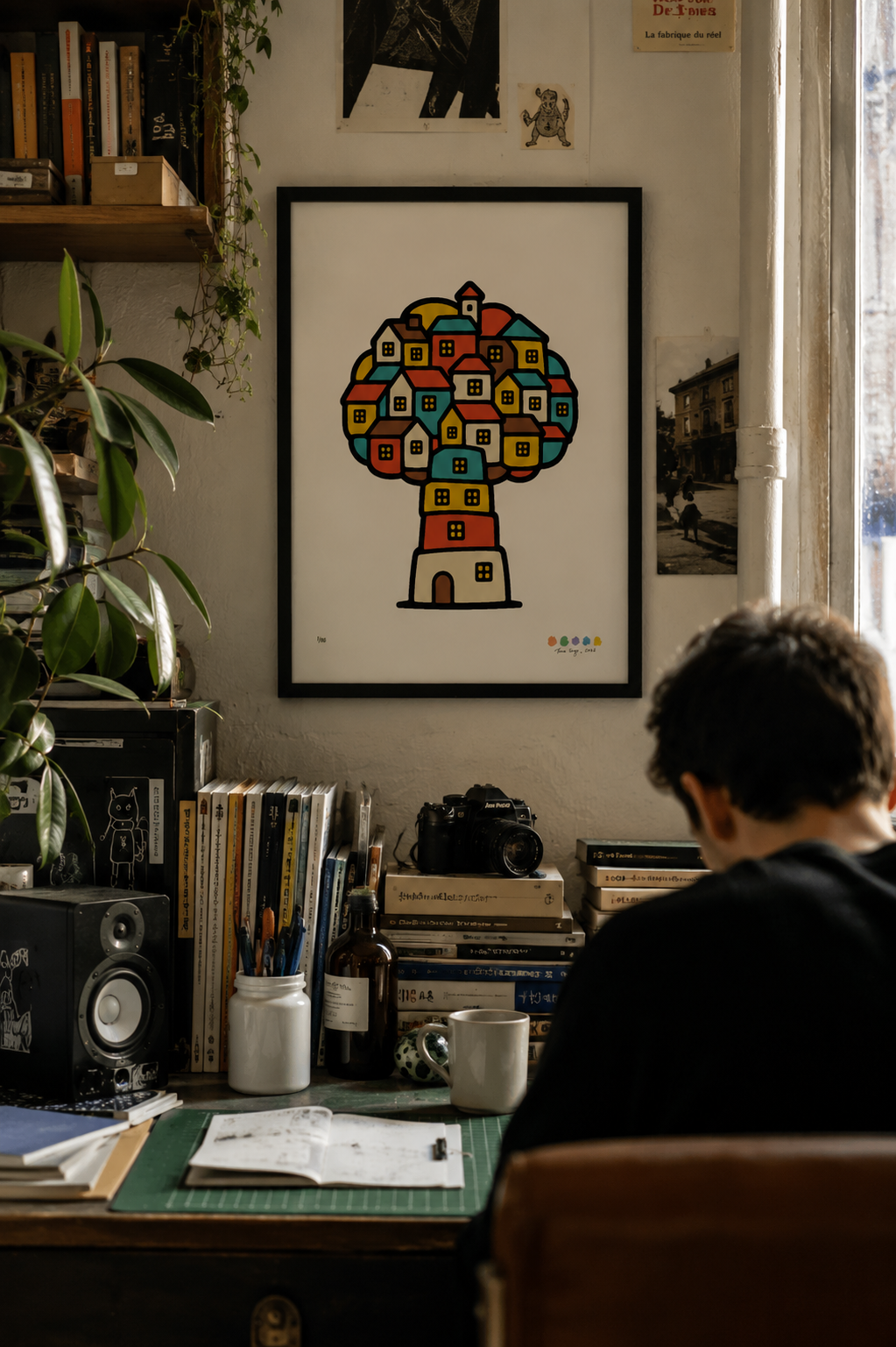 Framed Treehouse Homes artwork hanging above a cluttered desk in an inhabited creative studio.