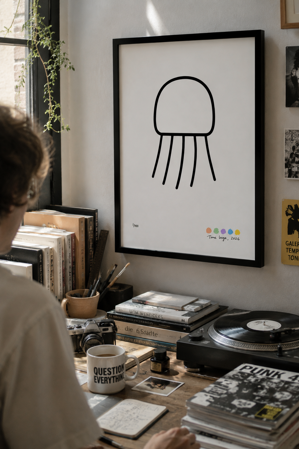 Black-framed Nimbus Jellyfish art print hanging above a lived-in desk filled with books, records and creative objects.