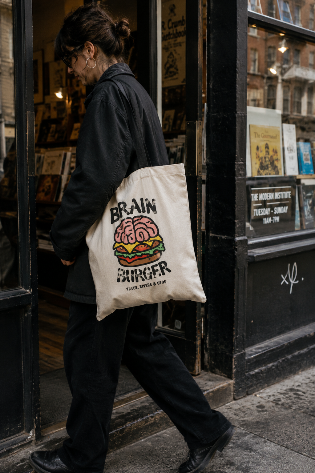 Person leaving an independent shop carrying a cream Trees, Rivers & UFOs Brain Burger tote bag at their side.