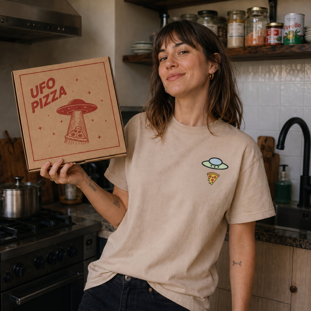 Woman wearing the sand Trees, Rivers & UFOs Forest Pizza Tee in a kitchen.