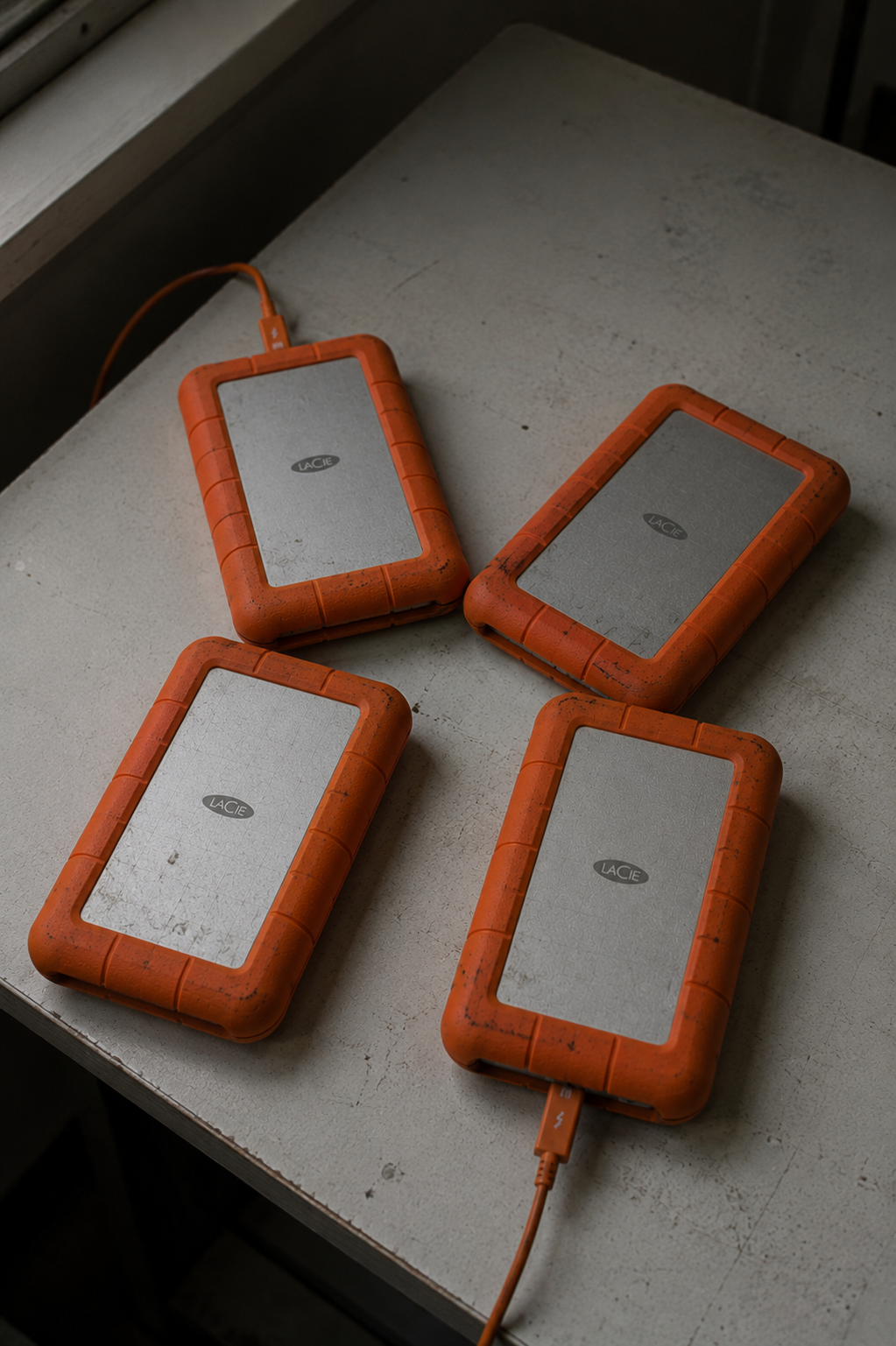 Four orange-cased external hard drives on a table beside a window.