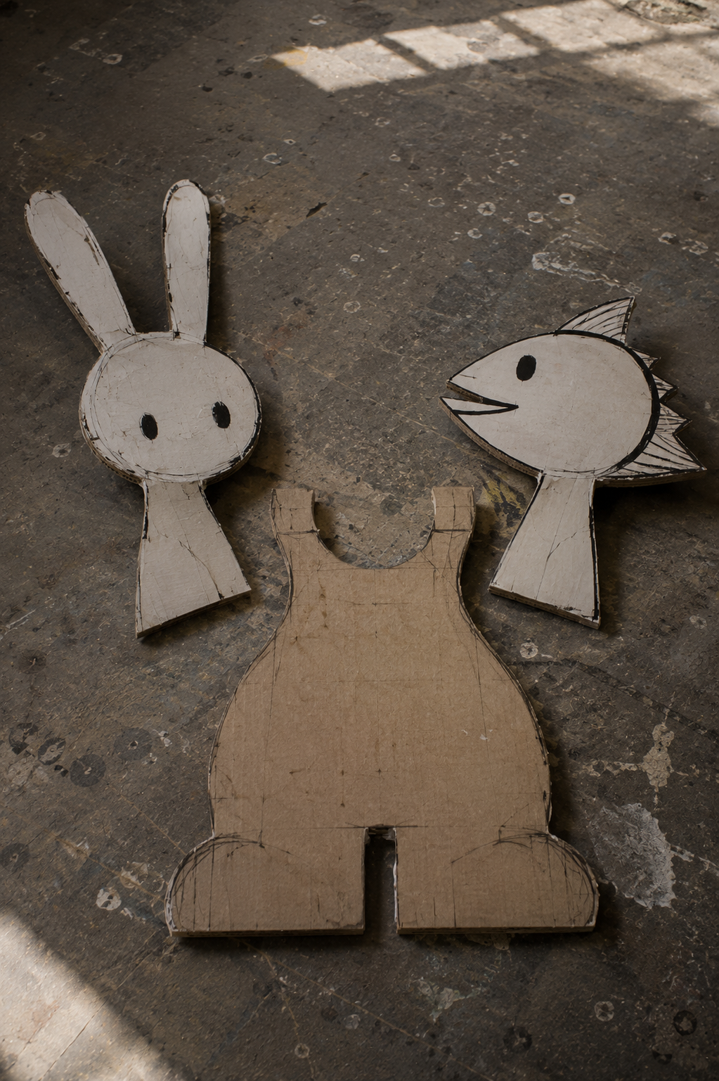 Separate cardboard rabbit head, fish head and body pieces arranged on a workshop floor.