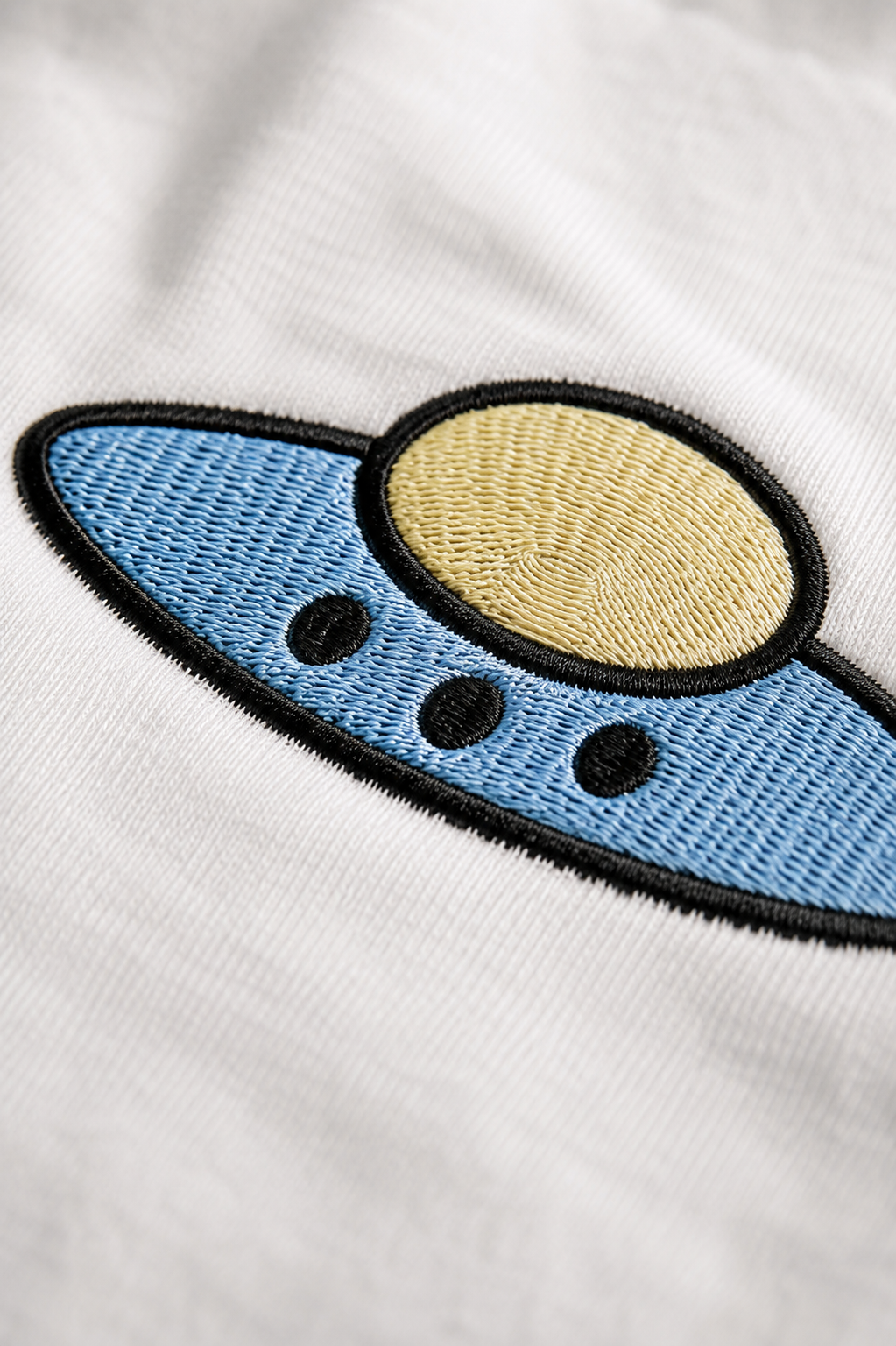 Close-up of blue and yellow UFO embroidery with a black outline on white fabric.