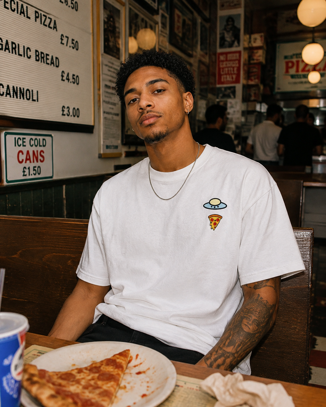 Person wearing a white UFO-and-pizza T-shirt while seated in a pizza restaurant.