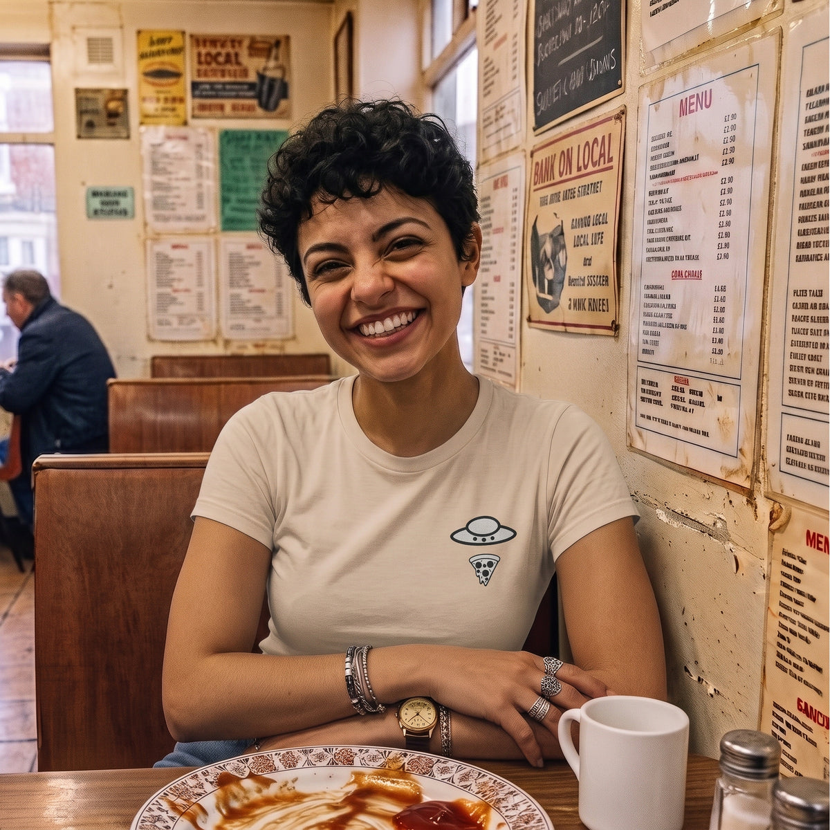Woman wearing the sand Trees, Rivers & UFOs Nimbus Pizza Tee while seated in a diner booth.