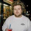 Person wearing the white Trees, Rivers & UFOs Nimbus Sweatshirt on a city street at night while holding a red cup.