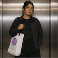 Woman carrying the Trees, Rivers & UFOs Orbit Jellyfish Tote Bag with purple jellyfish artwork in an elevator.